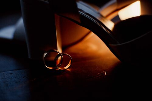 Free Close-up of wedding rings and high heels against a warm, dramatic backdrop. Stock Photo