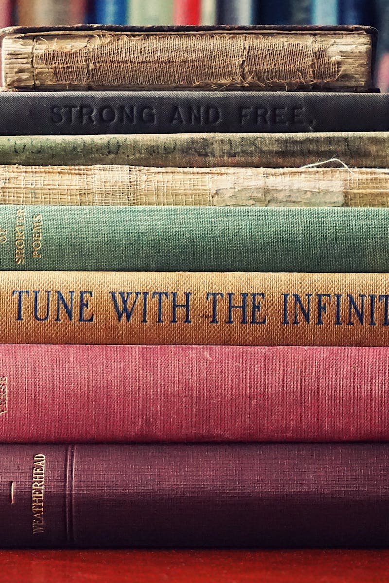 A stack of vintage hardcover books on a wooden table in a cozy library setting. A stack of vintage hardcover books on a wooden table in a cozy library setting.