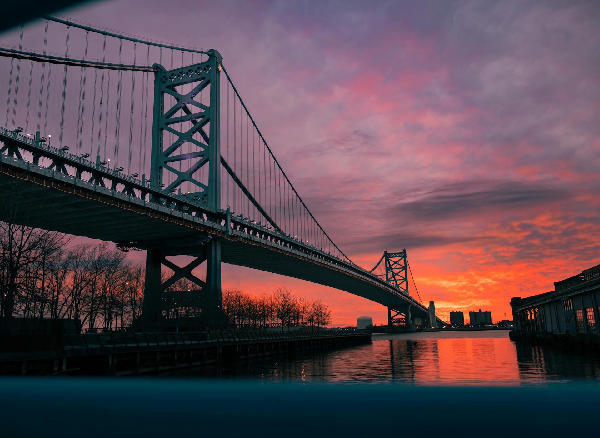 A stunning sunset view of the Benjamin Franklin Bridge in Philadelphia, with vivid orange and purple skies.
