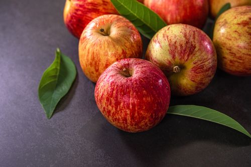 Free Close-up of fresh red apples with green leaves on a dark surface, highlighting their natural color and texture. Stock Photo