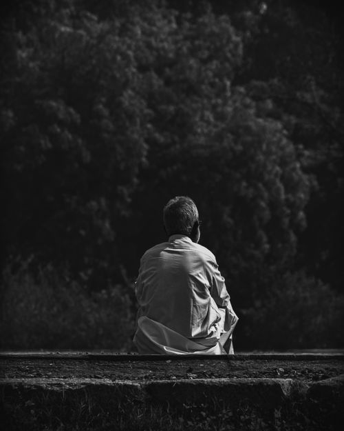 Free A man sitting outdoors, captured in black and white, emphasizing solitude and reflection. Stock Photo