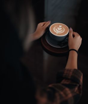 A woman holding a cup of coffee with intricate latte art in a warm, cozy setting.