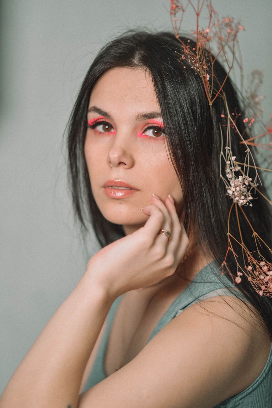 Portrait of a young woman with striking pink makeup and delicate floral accents, conveying elegance.