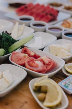 Close-up of Mediterranean appetizers with tomatoes, cheese, and lemon slices served on a wooden table.
