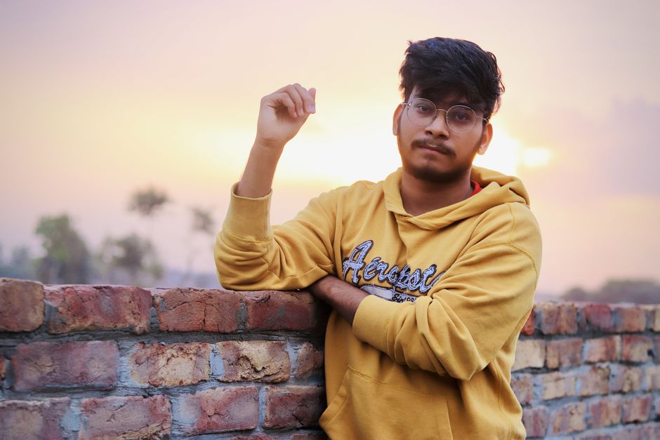 Midjourney vs Adobe Firefly: Marketing Visuals Face-Off (2024) Portrait of a young man in a yellow hoodie posing casually by a brick wall at sunset.