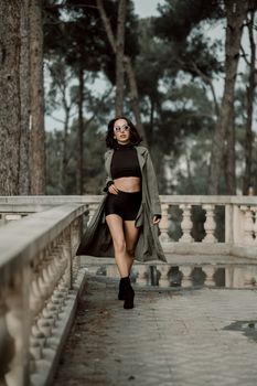 Woman in fashionable attire walking confidently outdoors with sunglasses.