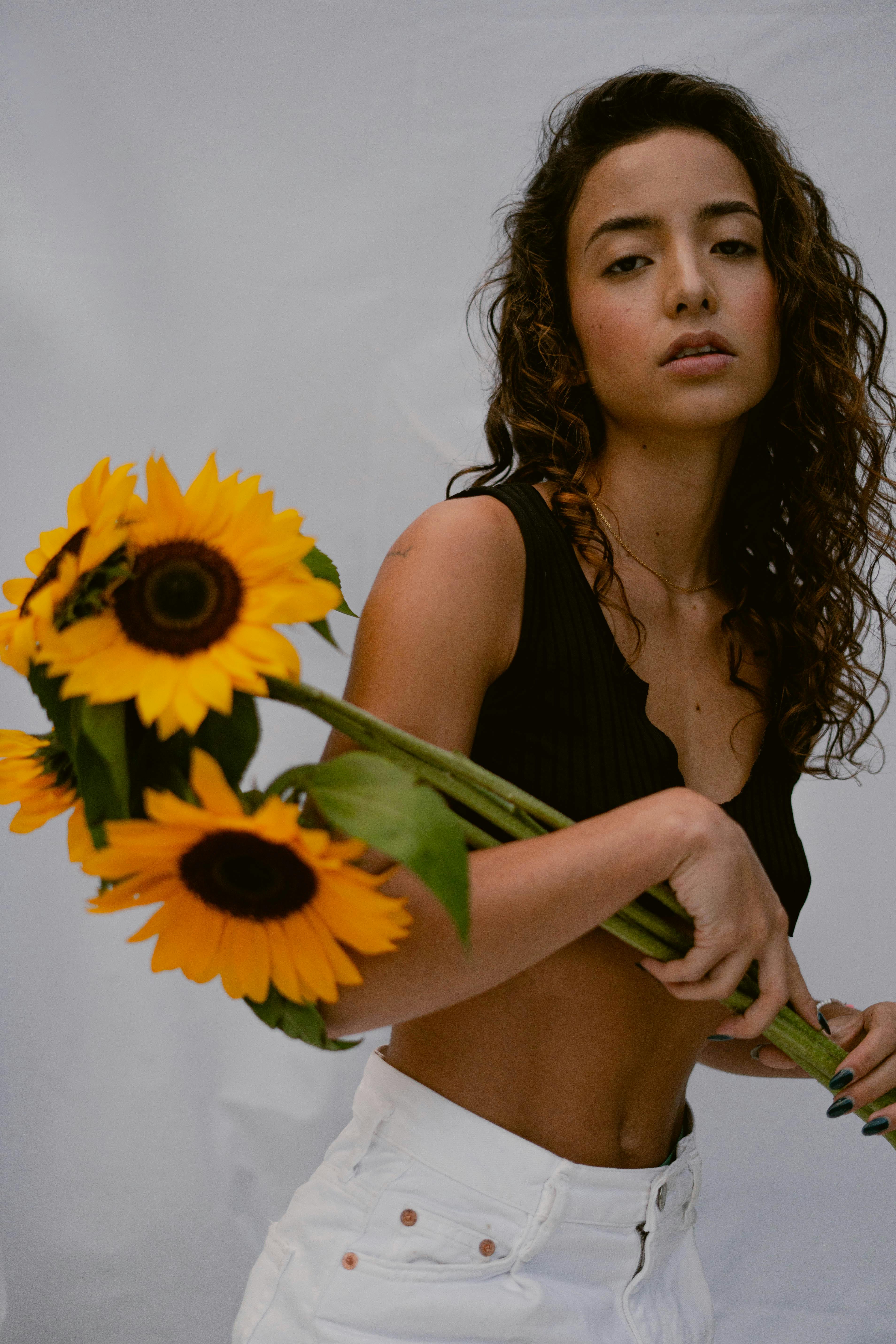 Stylish woman with curly hair posing indoors holding vibrant sunflowers.