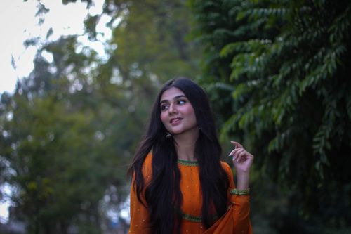 Free Portrait of a smiling woman in an orange outfit with long hair outdoors. Stock Photo