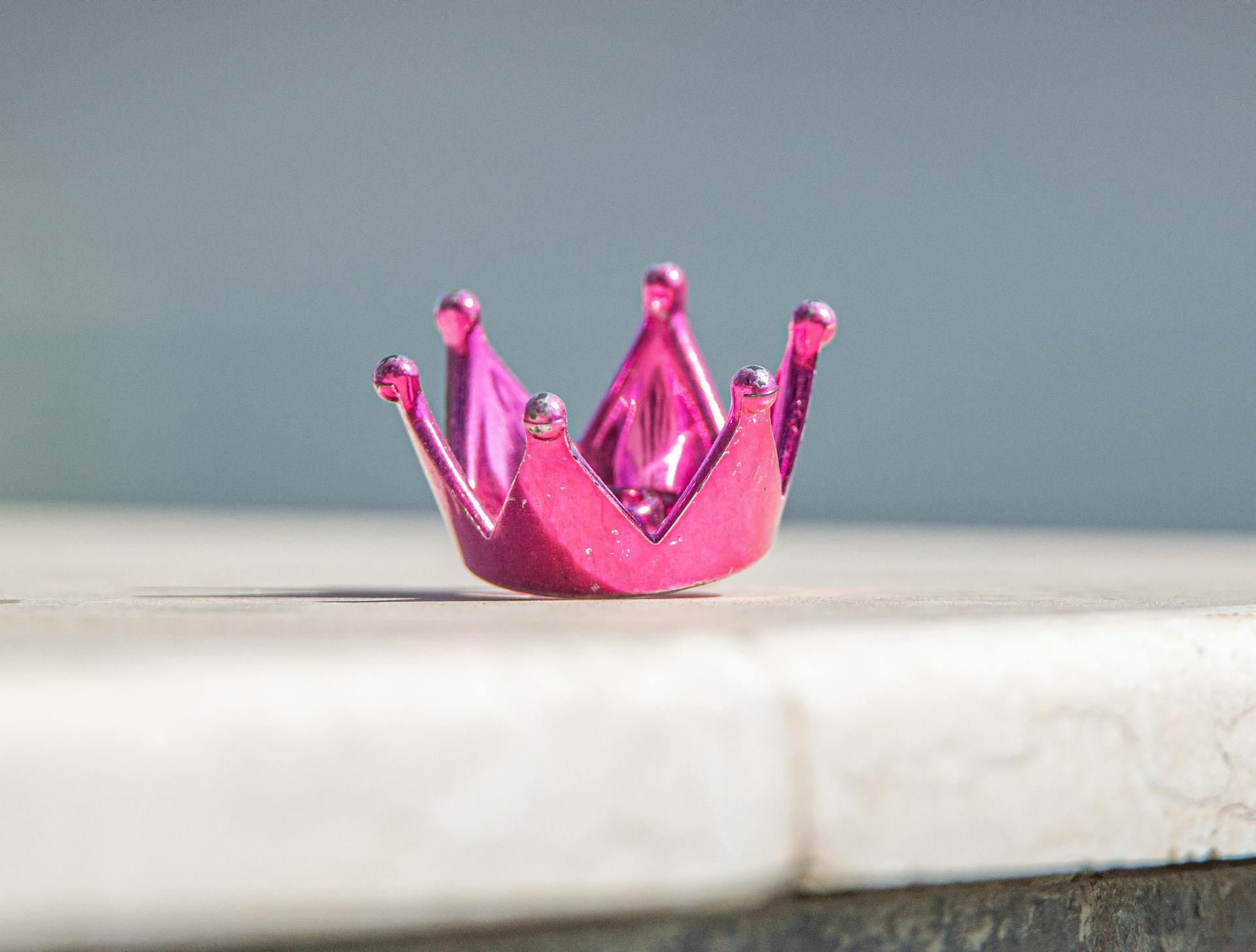 A shiny pink miniature crown in a still life setting with bright lighting.