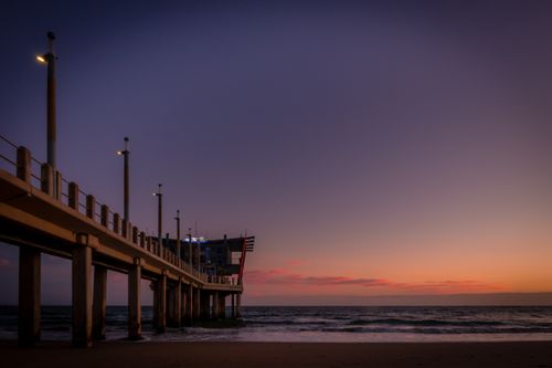 Free Stunning view of a pier at sunset on Durban beach, South Africa. Calm sea and vibrant sky. Stock Photo