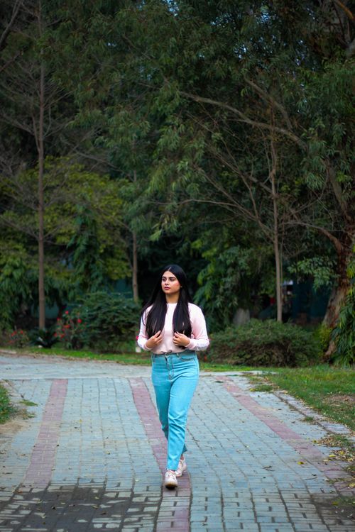 Free A young woman strolls through a serene forest park pathway on a peaceful day. Stock Photo