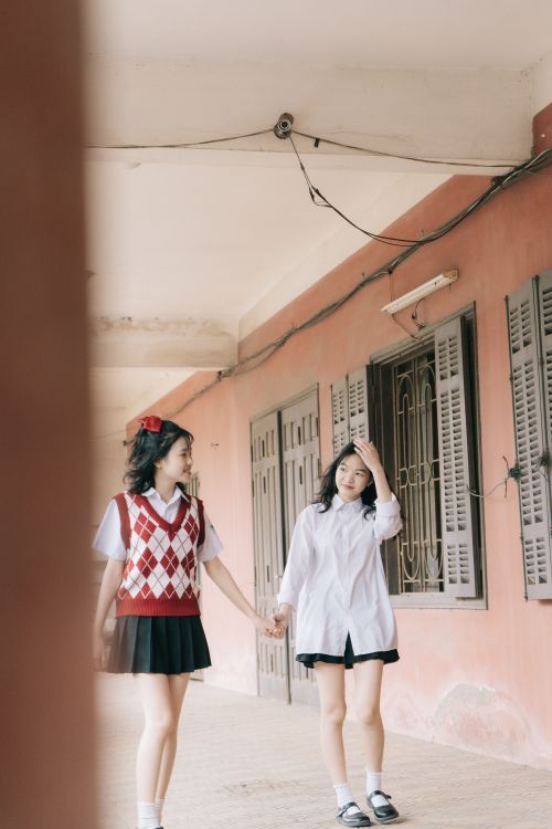 Free Two teenage girls in school uniforms walking hand in hand down a corridor. Stock Photo