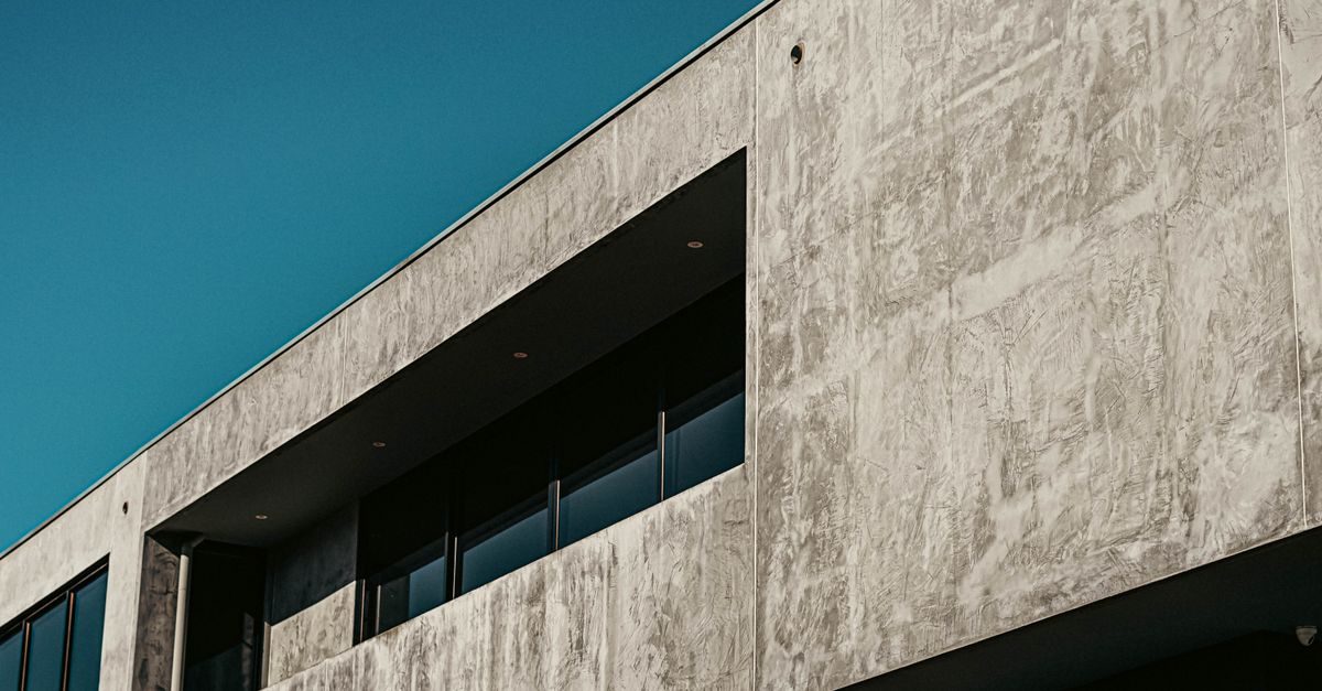 A minimalist concrete building facade featuring modern architectural design and large windows.