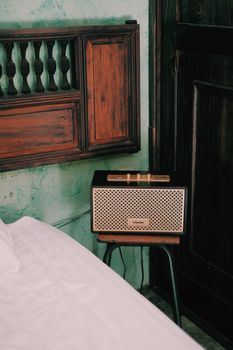 A retro radio resting on a stool beside a bed in a rustic bedroom setting.