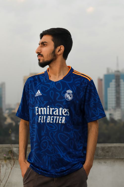 Free Profile shot of a man in a blue football jersey, standing on a terrace with city skyline in the background. Stock Photo