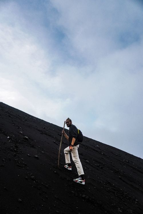 Free A determined hiker climbs a steep volcanic slope under a vast blue sky, embodying adventure. Stock Photo