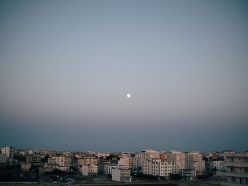 Free A serene aerial view of a cityscape under the evening sky with the moon visible. Stock Photo