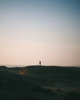 A lone person stands atop a desert hill under a twilight sky, creating a silhouette.