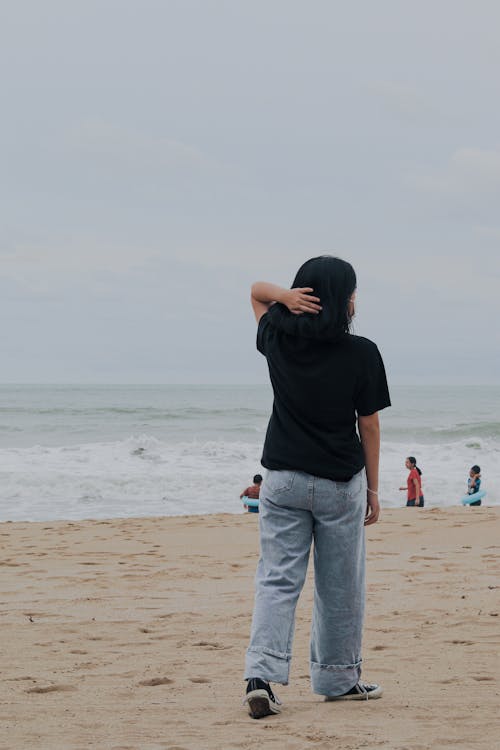 Free Man in Black Shirt and Blue Denim Jeans Standing on Beach Stock Photo