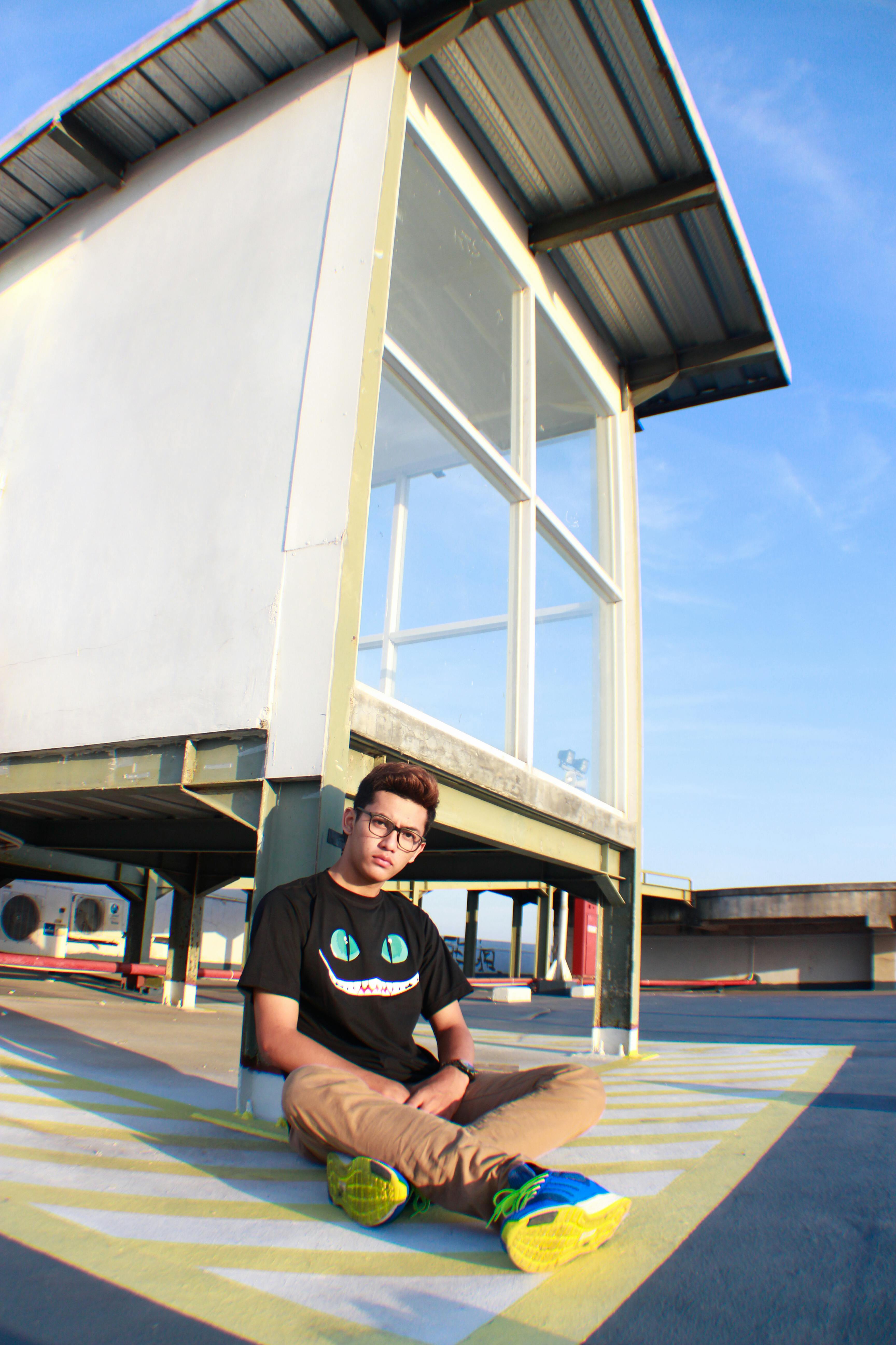 Young man sitting on an urban rooftop near a modern glass structure on a sunny day.
