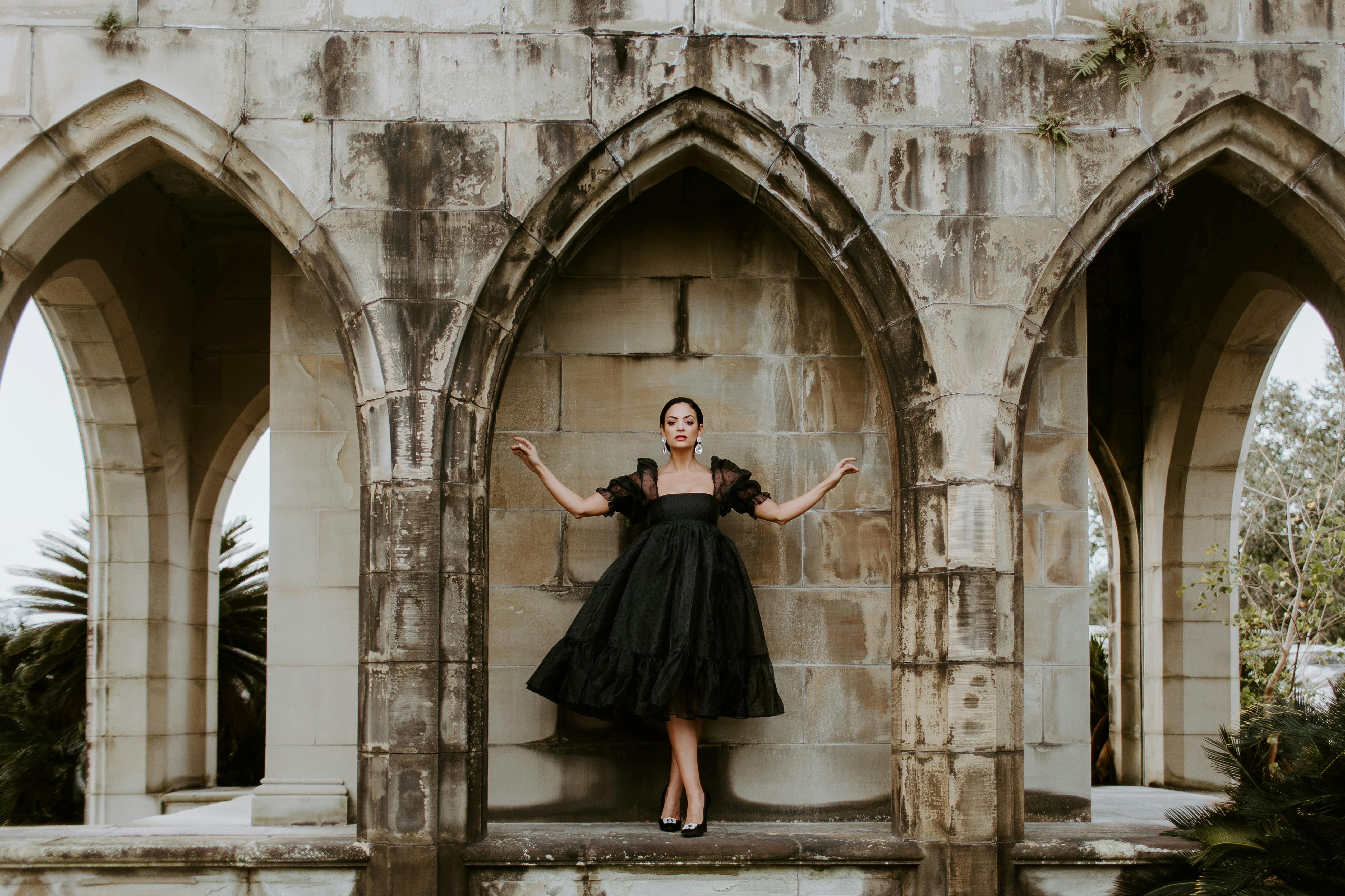 A woman in a black dress poses amid gothic arches outdoors in New Orleans.