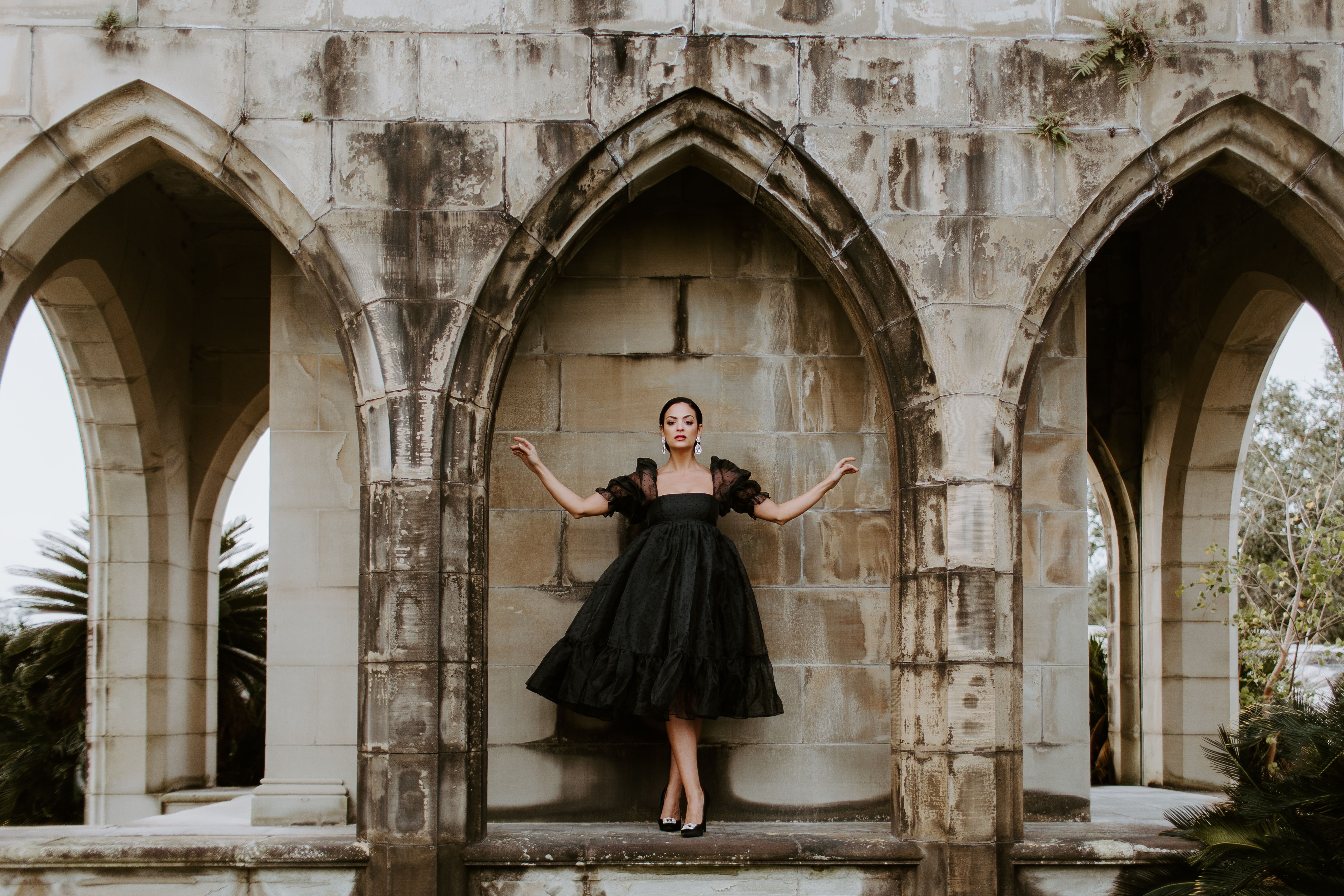 Elegant woman wearing a black dress standing under stone arches in a grey stone building