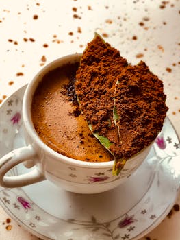 A close-up of espresso in a floral porcelain cup with ground coffee on a leaf.