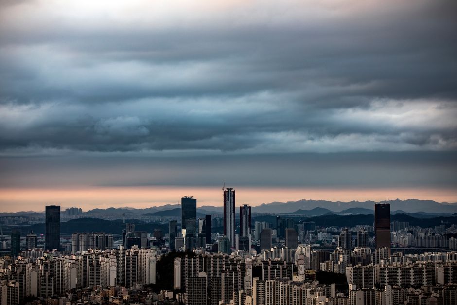 A panoramic view of Seoul's skyline at twilight with dramatic clouds and city lights coming on.