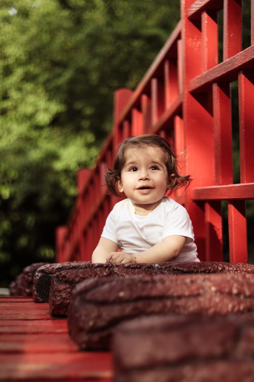 Baby Draagt Wit Shirt Met Ronde Hals Naast Rode Houten Hek