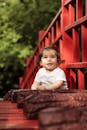 可爱的小孩坐在一座红色的桥上，享受着户外阳光明媚的一天