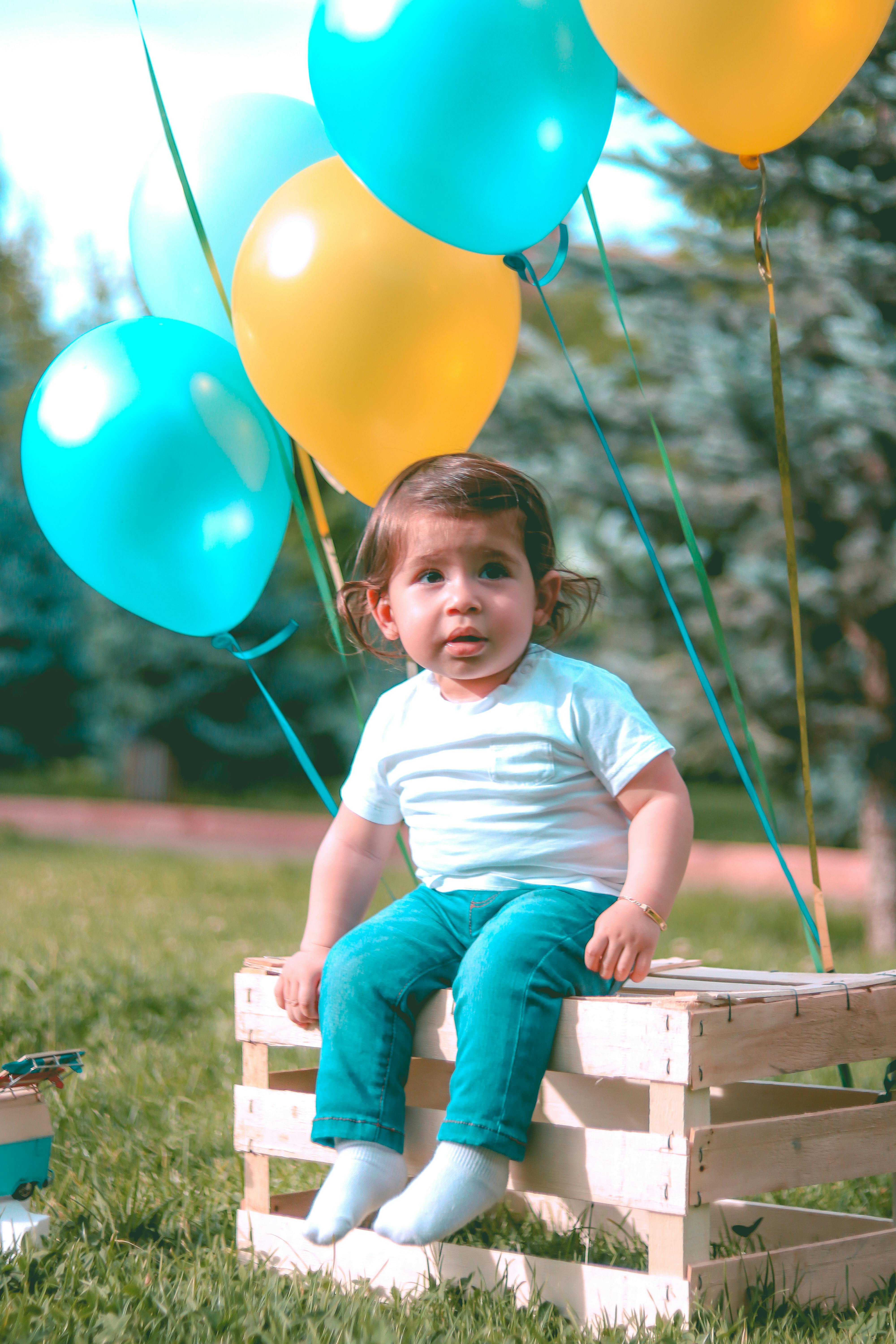 一个可爱的蹒跚学步的孩子坐在阳光明媚的公园里，身旁是一个气球板条箱