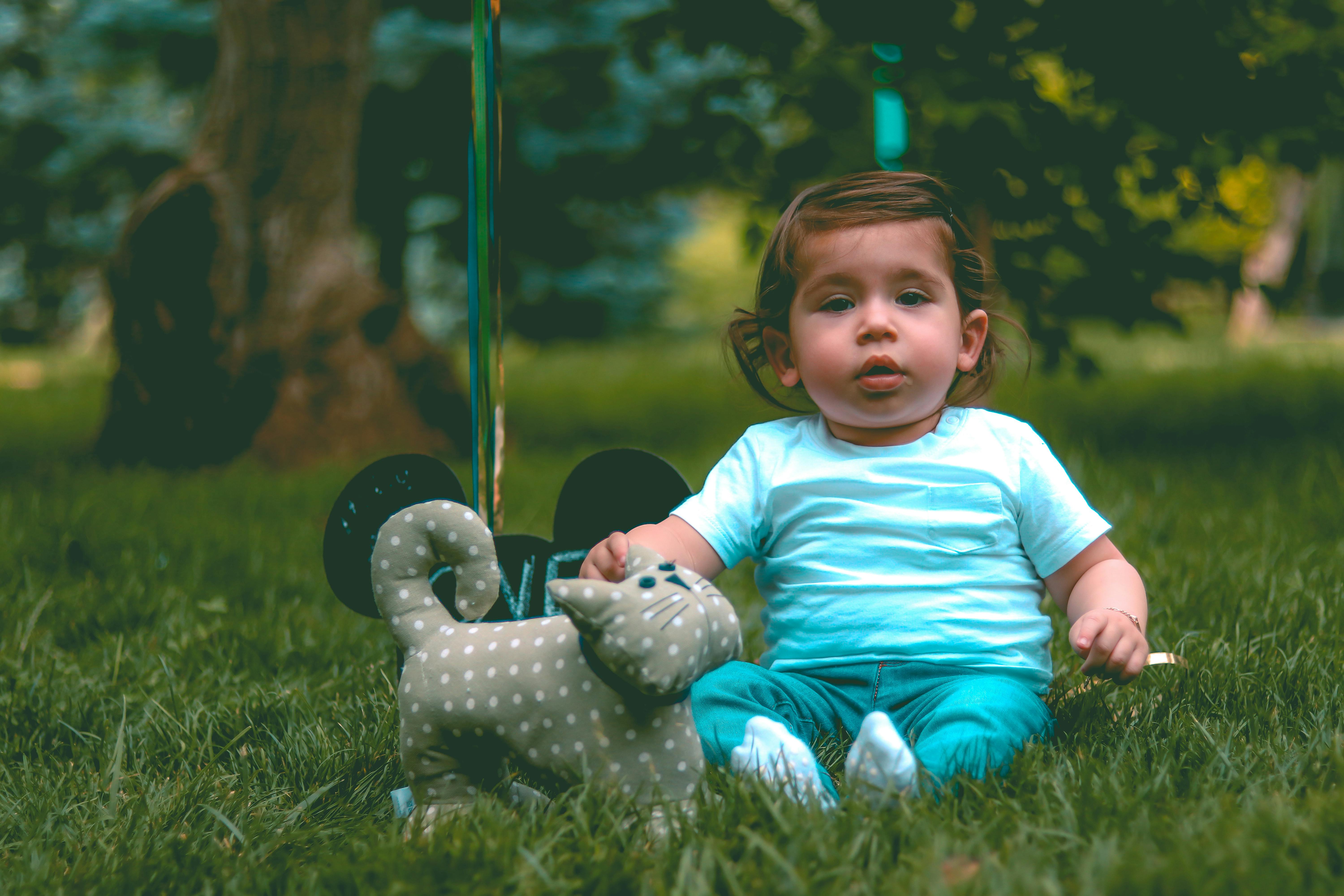 Toddler Wearing Teal Tshirt and Teal Pants Beside Gray Cat Plush Toy