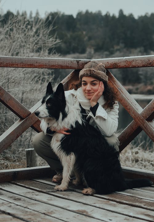 Woman in White Long Sleeve Shirt Sitting Beside a Border Collie