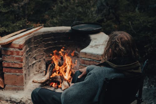 A Person in Gray Jacket Sitting Beside a Fire Pit