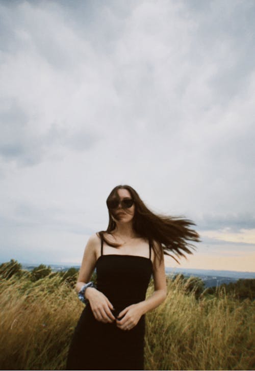 Woman in Black Spaghetti Strap Dress with Black Sunglasses Standing on Grass Field