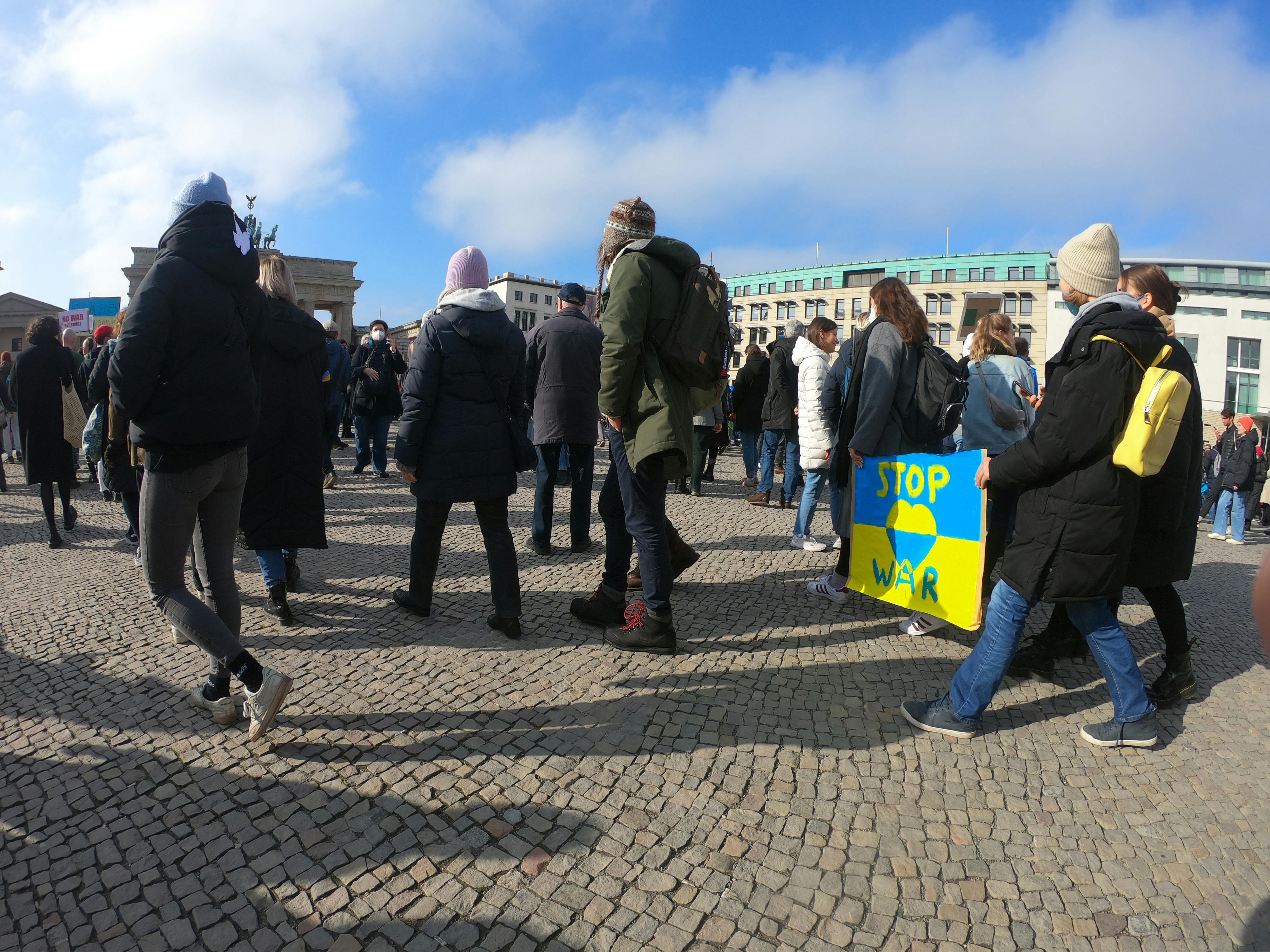 Demonstrators protest for peace in Berlin's famous public square, holding signs against war.