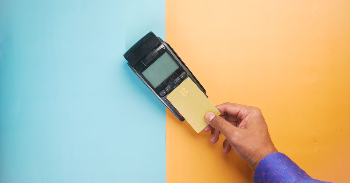 A hand tapping a credit card on a payment terminal for a contactless transaction.