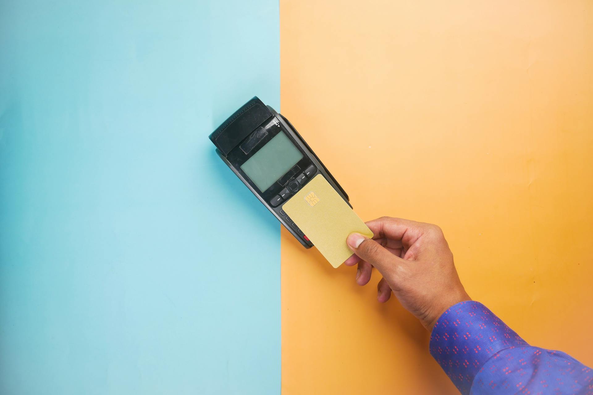 A hand tapping a credit card on a payment terminal for a contactless transaction.