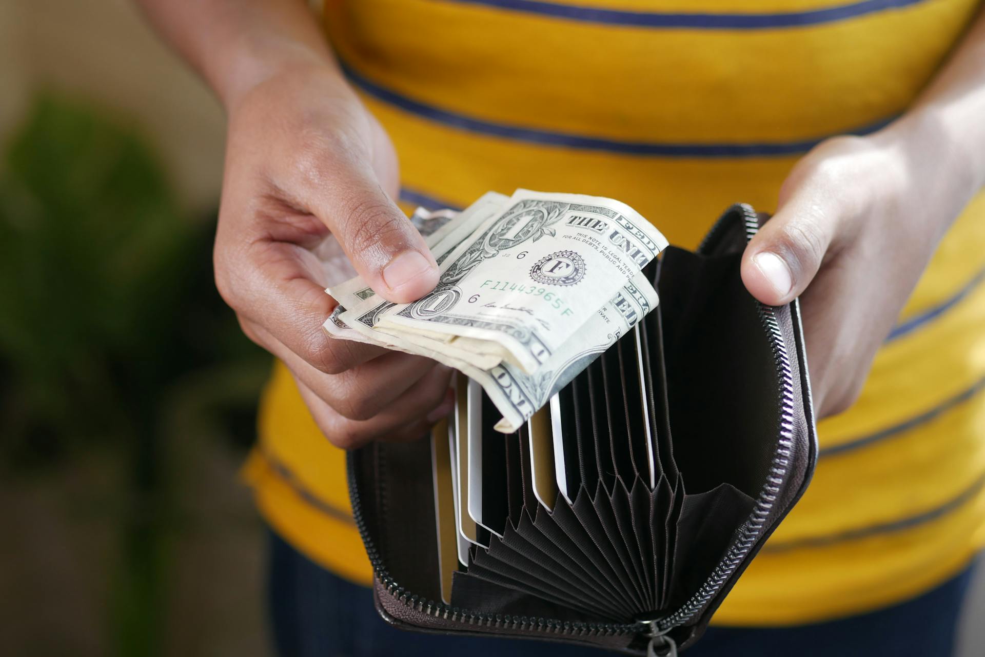 Close-up of a person's hands holding US dollar bills and a wallet.