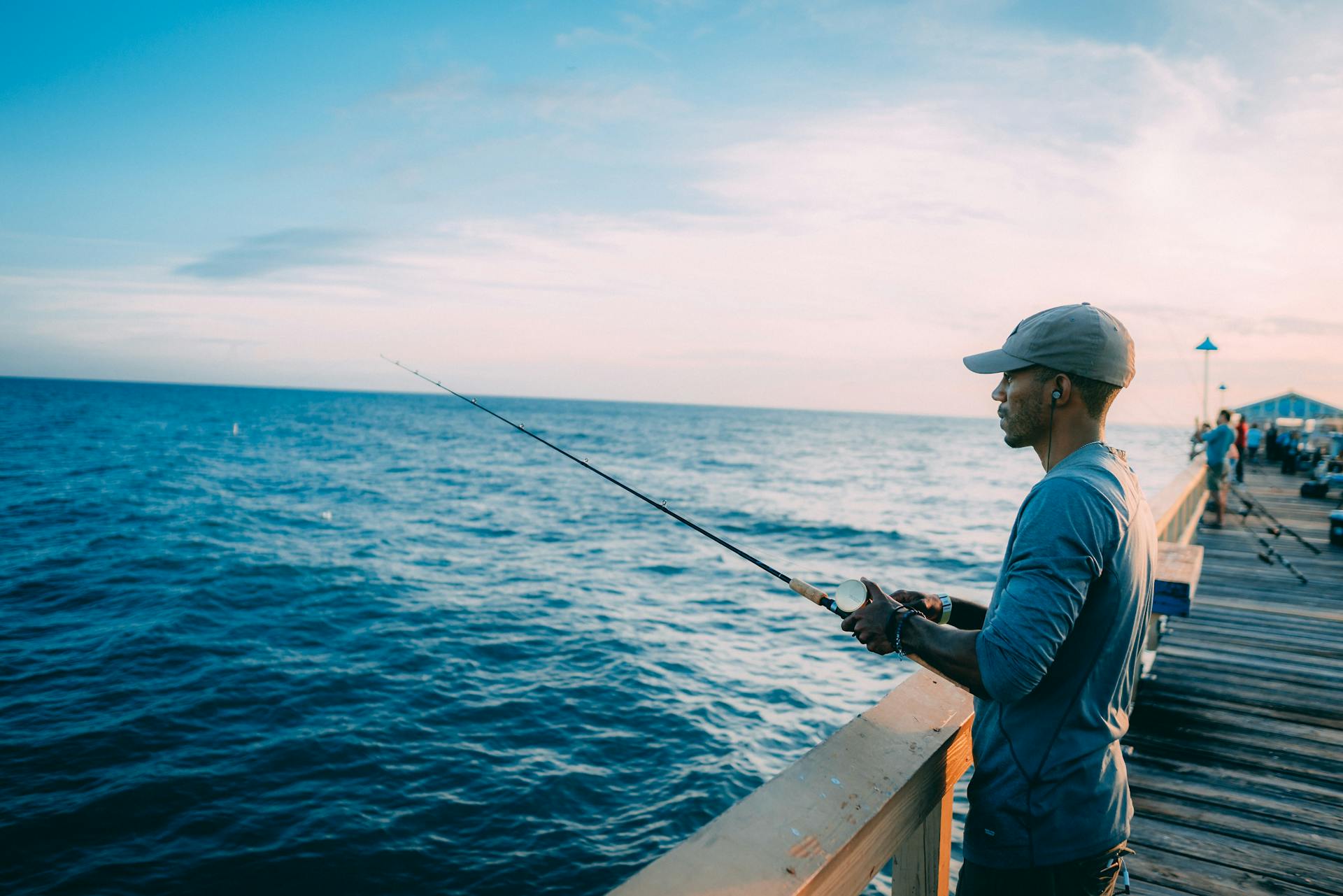 A man enjoys fishing on a sunny Florida pier, surrounded by the ocean's calm waters.