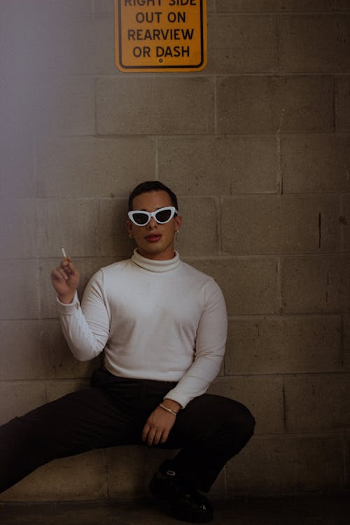 Free Man in White Sweater and Black Pants Wearing White Sunglasses While Smoking a Cigarette Stock Photo