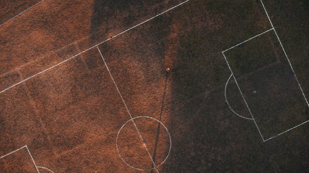 Aerial drone shot of a soccer field, highlighting markings and textures at dusk.