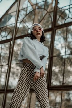 Trendy young woman in a hoodie and checkered pants poses fashionably indoors.