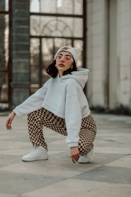 Stylish female model posing with attitude, wearing cropped hoodie and checkered pants in urban backdrop.