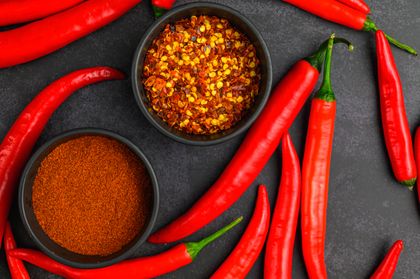 Crushed chile flakes in a dark bowl beside fresh chiles. Photo by Jana Ohajdova on Pexels.