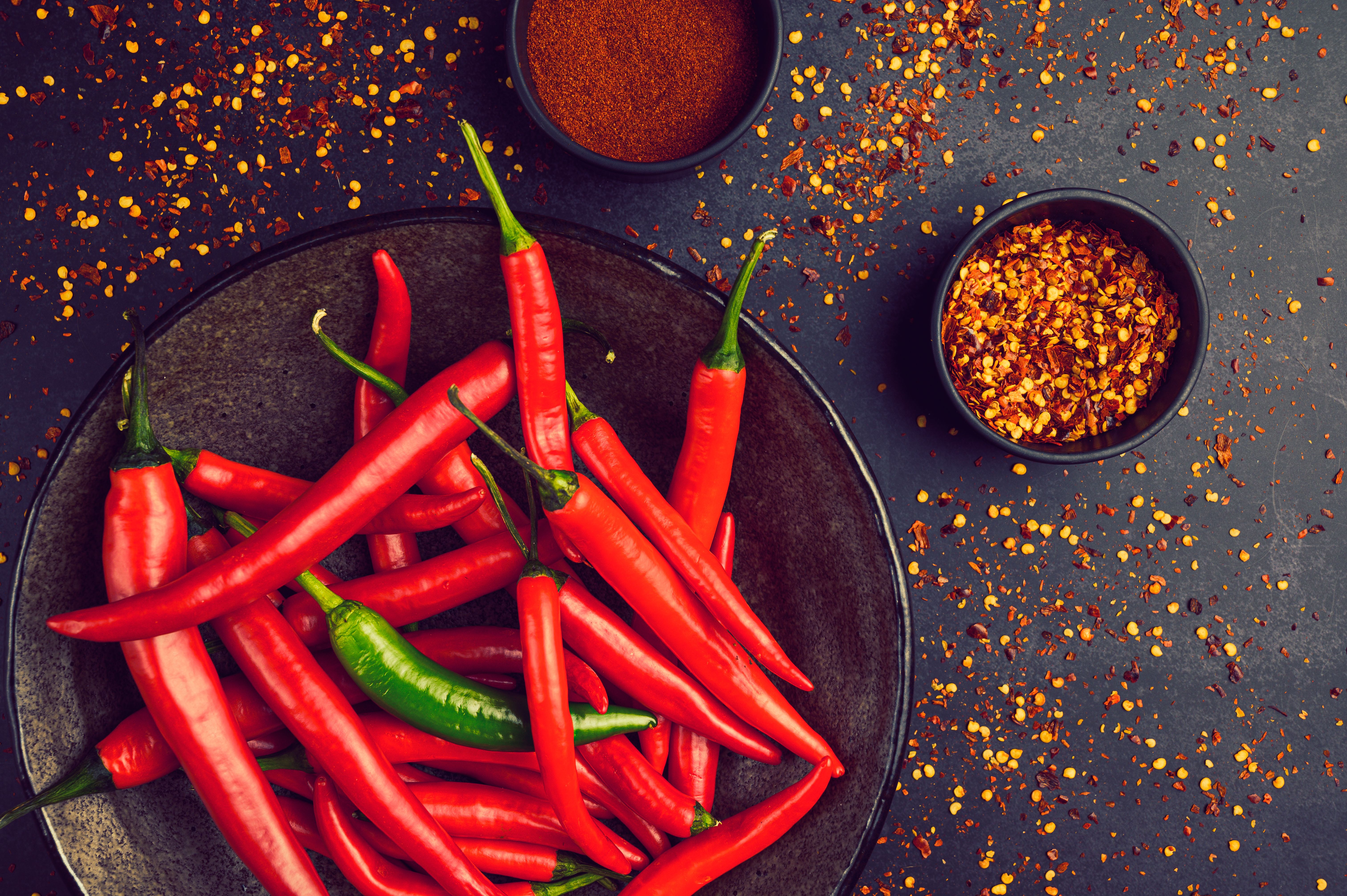 Close-up of fresh red and green chili peppers in a bowl with spices and pepper flakes.