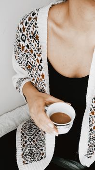 Close-up of a woman holding a cup of Turkish coffee, wearing a patterned knitted cardigan.