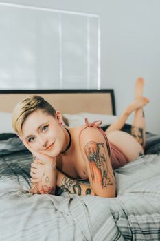 Captivating image of a tattooed woman in lingerie lying on a bed indoors, exuding a modern boudoir vibe.