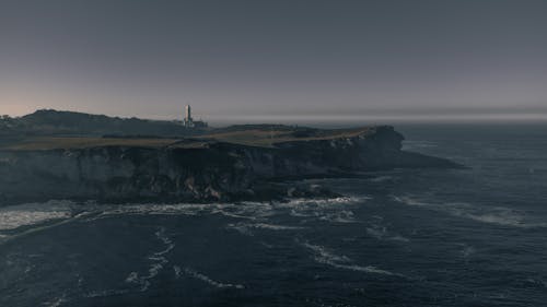 White Lighthouse on Brown Rock Formation Beside the Sea