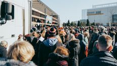A large crowd gathers outside near a truck, participating in a rally event in Vilnius.